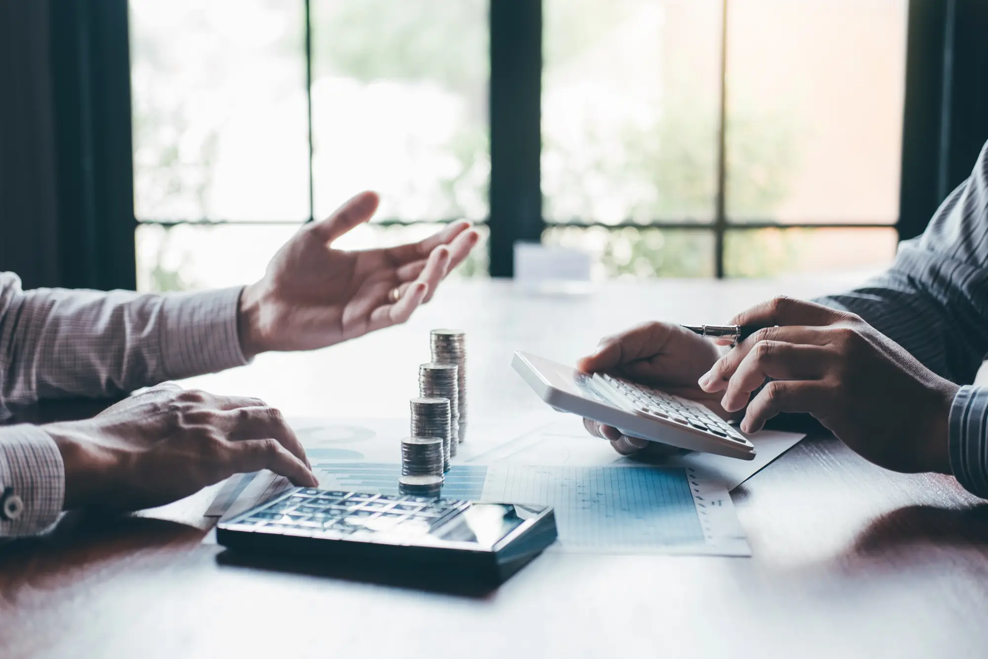 Two people discussing finances with calculators and stacks of coins.