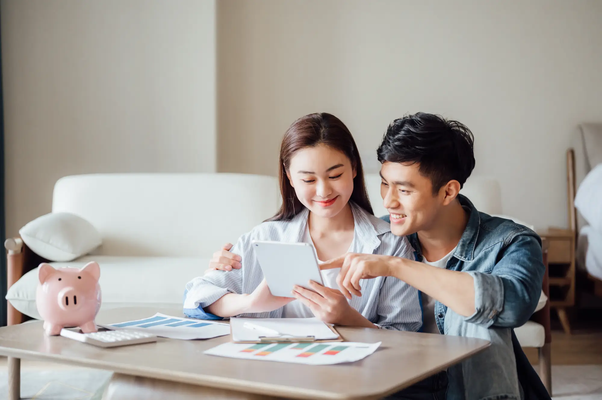 Smiling couple looking at a tablet with a piggy bank nearby.