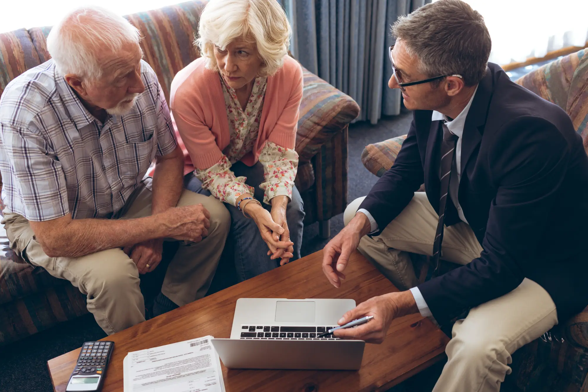 Three adults discussing documents and a laptop on a wooden table.