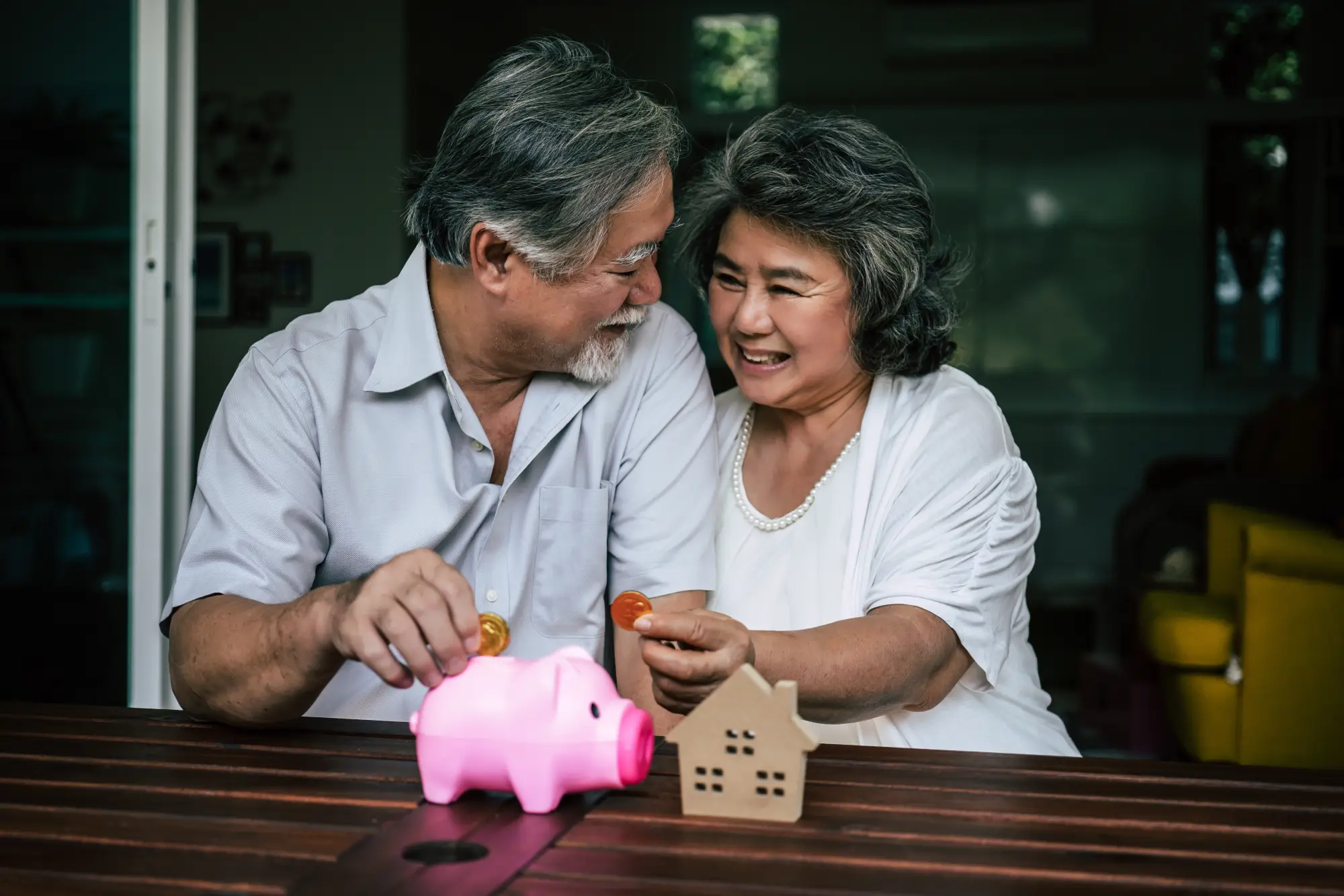 Smiling elderly couple saving money with a piggy bank and house model