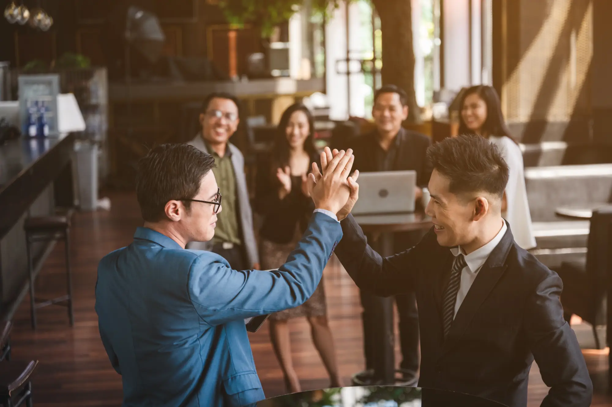 Two men in suits giving a high-five, celebrating success in an office.